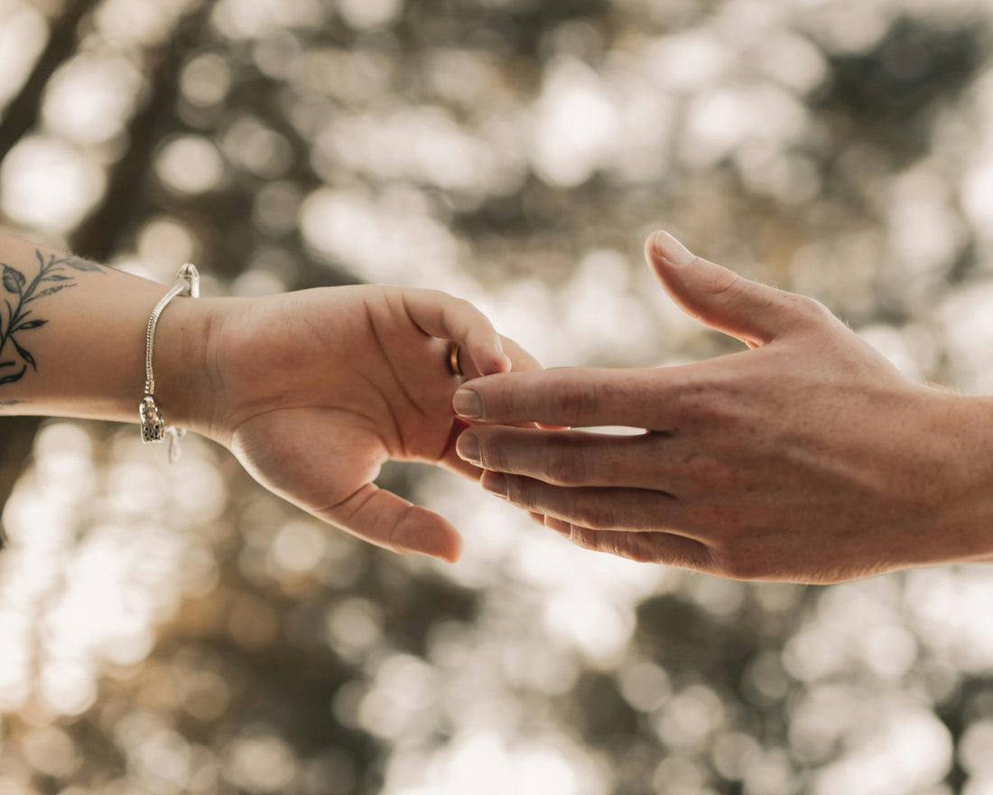 Two hands reaching towards each other with a blurred natural background